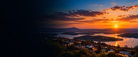 Sunset over a Queensland hinterland valley, with a river, islands and a distant coastal skyline catching the last of the light